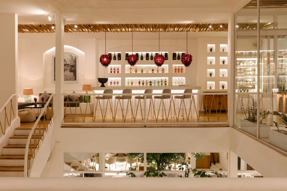 Interior view of Mauri Restaurant featuring a minimalist white bar, rustic twig ceiling, and four iconic red pendant lights